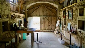 A rustic barn interior with wooden beams, stone walls, and artwork. - Authentic country house in Tannay with garden (Tannay)