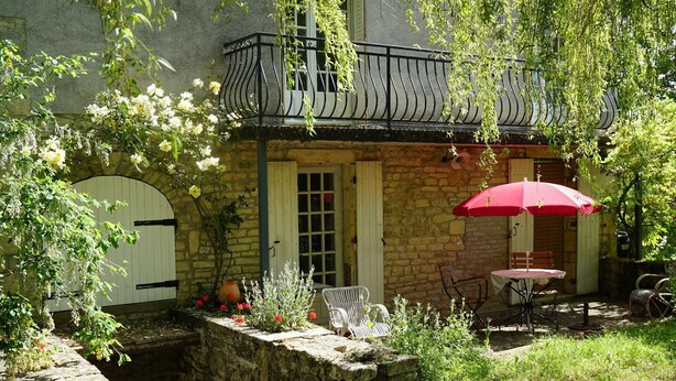 A stone building with a balcony, a small table with a red umbrella, and a chair. - Authentic country house in Tannay with garden (Tannay)