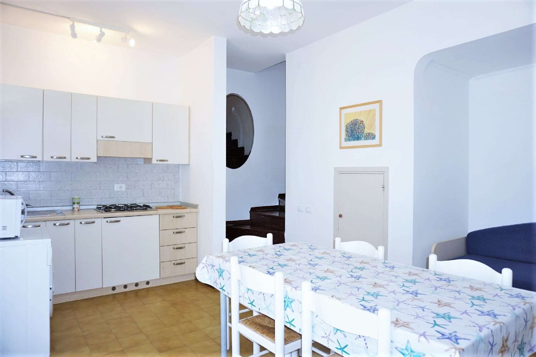 A compact kitchen with white cabinets and a dining table set with white chairs.