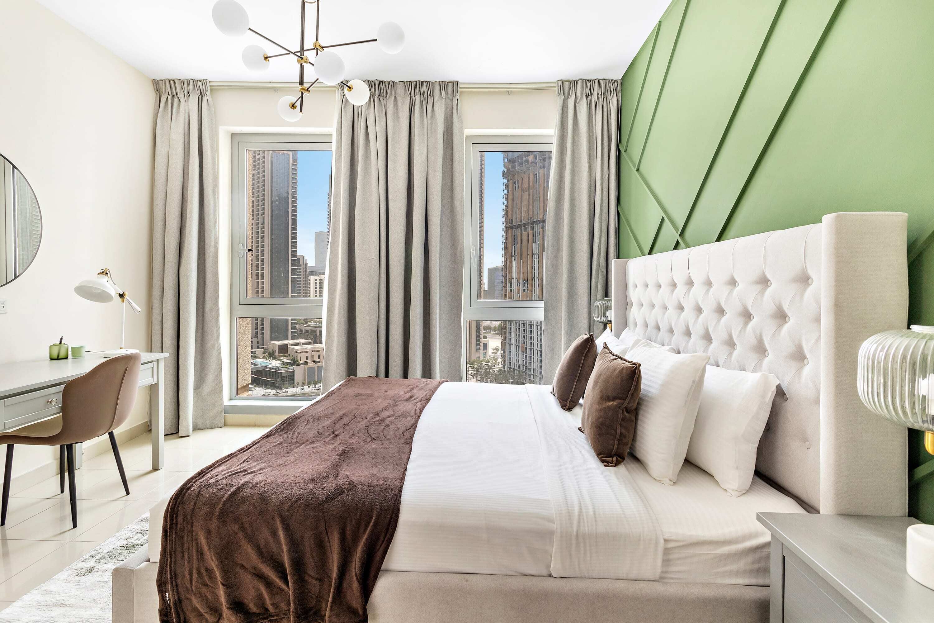 A modern bedroom with a large bed, a desk, and a view of tall buildings.
