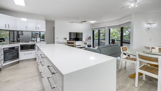 A modern kitchen with a large island, built-in appliances, and a dining area with a glass table and chairs. - Executive Unit in the Treetops (BONGAREE)