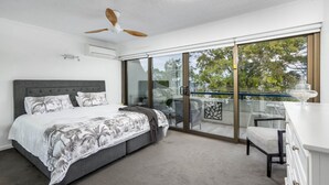 A bedroom with a bed, a ceiling fan, an air conditioning unit, and a sliding glass door leading to a balcony with outdoor furniture. - Executive Unit in the Treetops (BONGAREE)