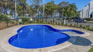 A swimming pool with a curved design, surrounded by a gravel area and a metal fence. - Executive Unit in the Treetops (BONGAREE)