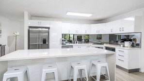 A modern kitchen with white cabinetry, stainless steel appliances, and a large island with bar stools. - Executive Unit in the Treetops (BONGAREE)