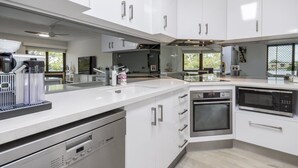 A modern kitchen with white cabinetry, stainless steel appliances, and a large window providing natural light. - Executive Unit in the Treetops (BONGAREE)