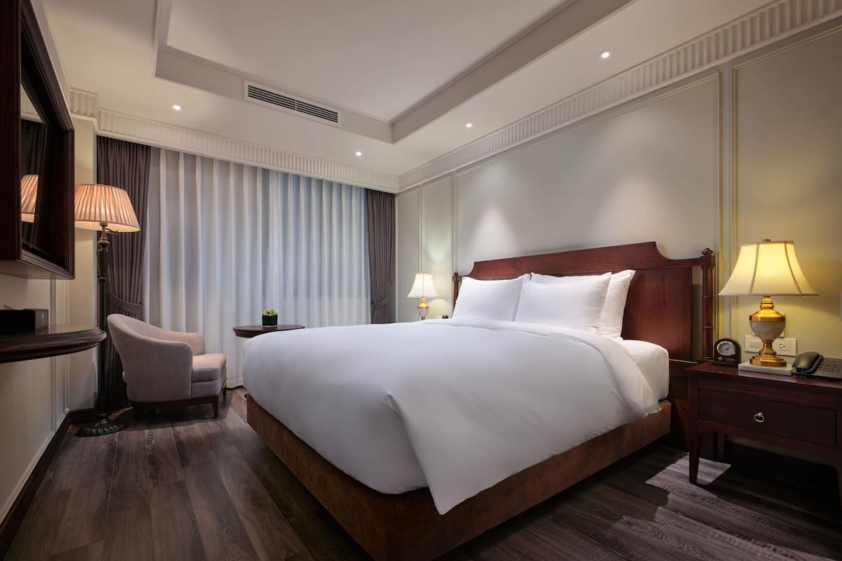 Une chambre d’hôtel avec un grand lit, un bureau avec une lampe, une chaise et une table de chevet avec une lampe.