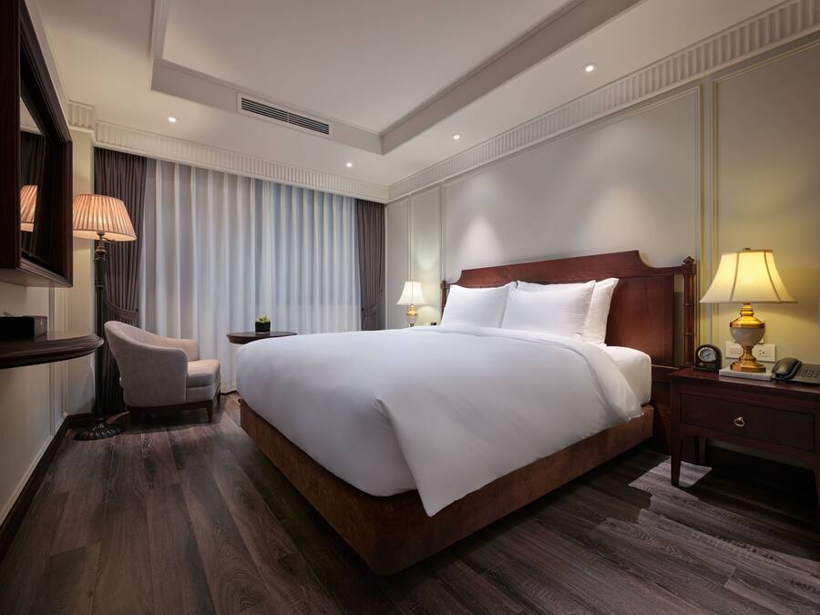 Habitación de hotel con una cama grande, un escritorio con lámpara, una silla y una mesita de noche con lámpara.