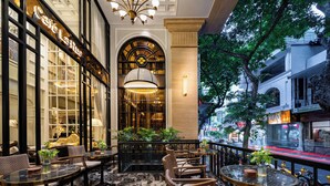 A well-lit indoor seating area with tables and chairs, large windows, and a view of the street outside. - GRAND HOTEL du LAC Hanoi (Hanoi)