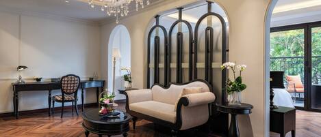 A luxurious room with a chandelier, a sofa, a desk, and a view of greenery outside.