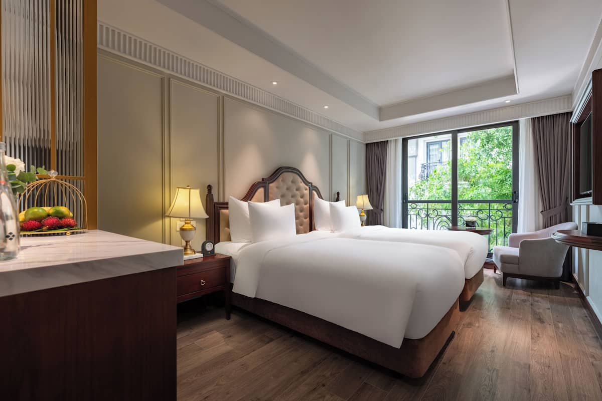 Une chambre d’hôtel avec un grand lit, une table de chevet avec une lampe, une chaise et une vue sur la verdure.