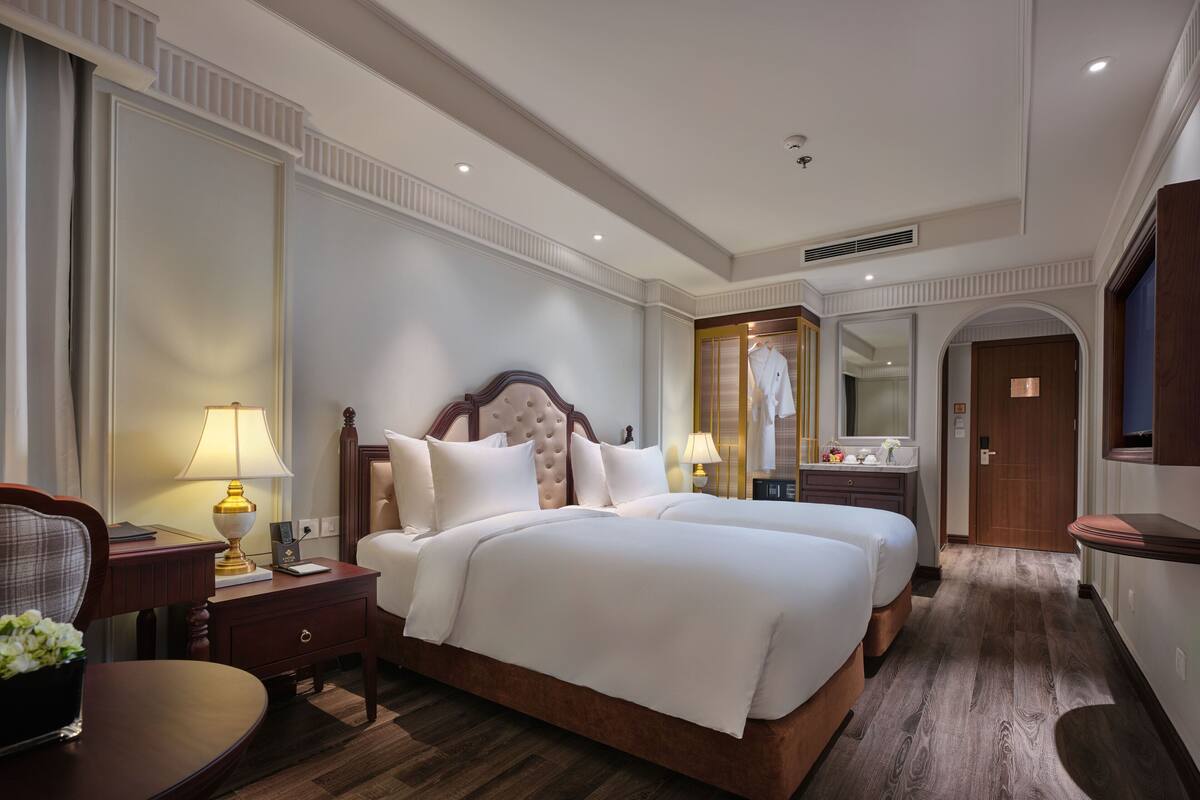 Une chambre d’hôtel avec un grand lit, une table de chevet avec une lampe, une chaise et une petite table sur laquelle est posé un vase de fleurs.