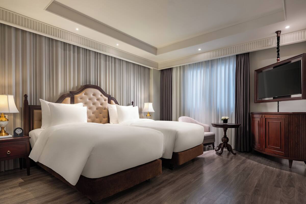 Une chambre d’hôtel avec un grand lit, deux tables de chevet avec des lampes, une télévision et une armoire en bois.