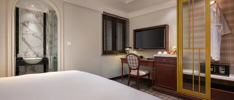 A hotel room with a large bed, a desk with a computer, a television, and a bathroom with a marble sink.