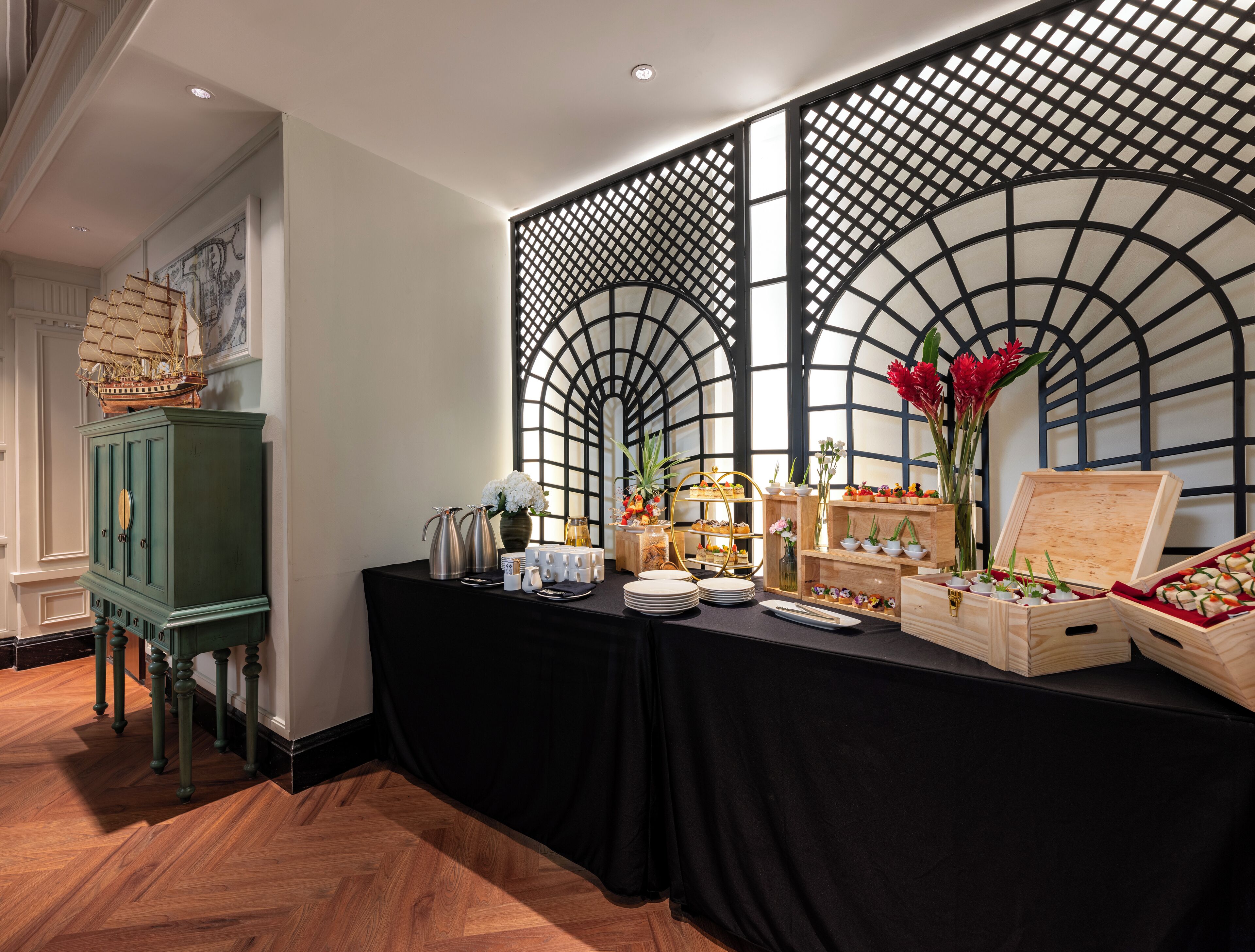 Un buffet proposant une variété de plats, une maquette de navire et des éléments décoratifs, le tout dans une pièce au plancher en bois et recouverte d’une nappe noire.