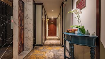 A hallway with marble walls, a wooden door at the end, and a blue console table with books and a potted plant.