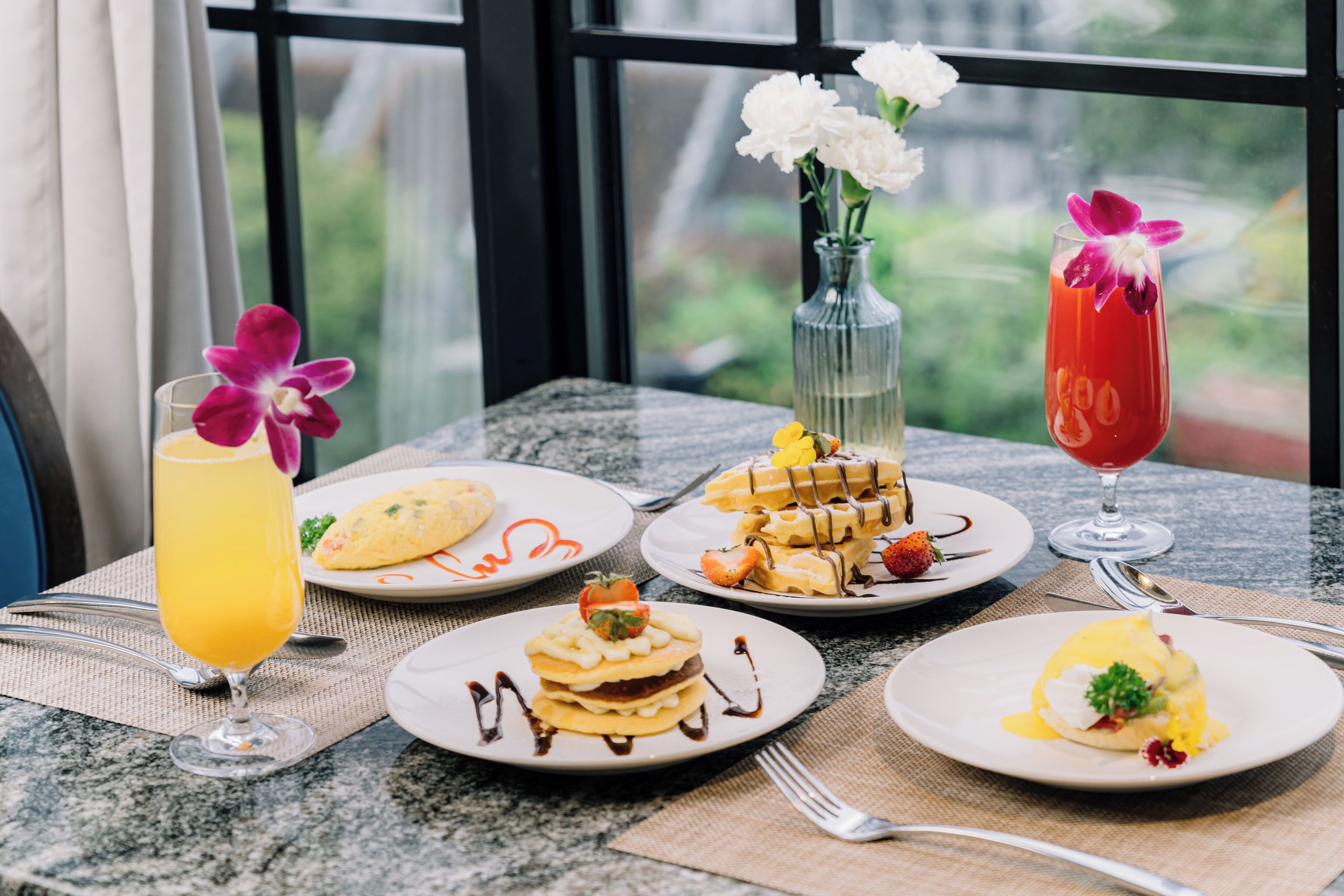 Une table garnie de différents plats pour le petit-déjeuner, notamment des gaufres, des crêpes et un verre de jus d’orange.