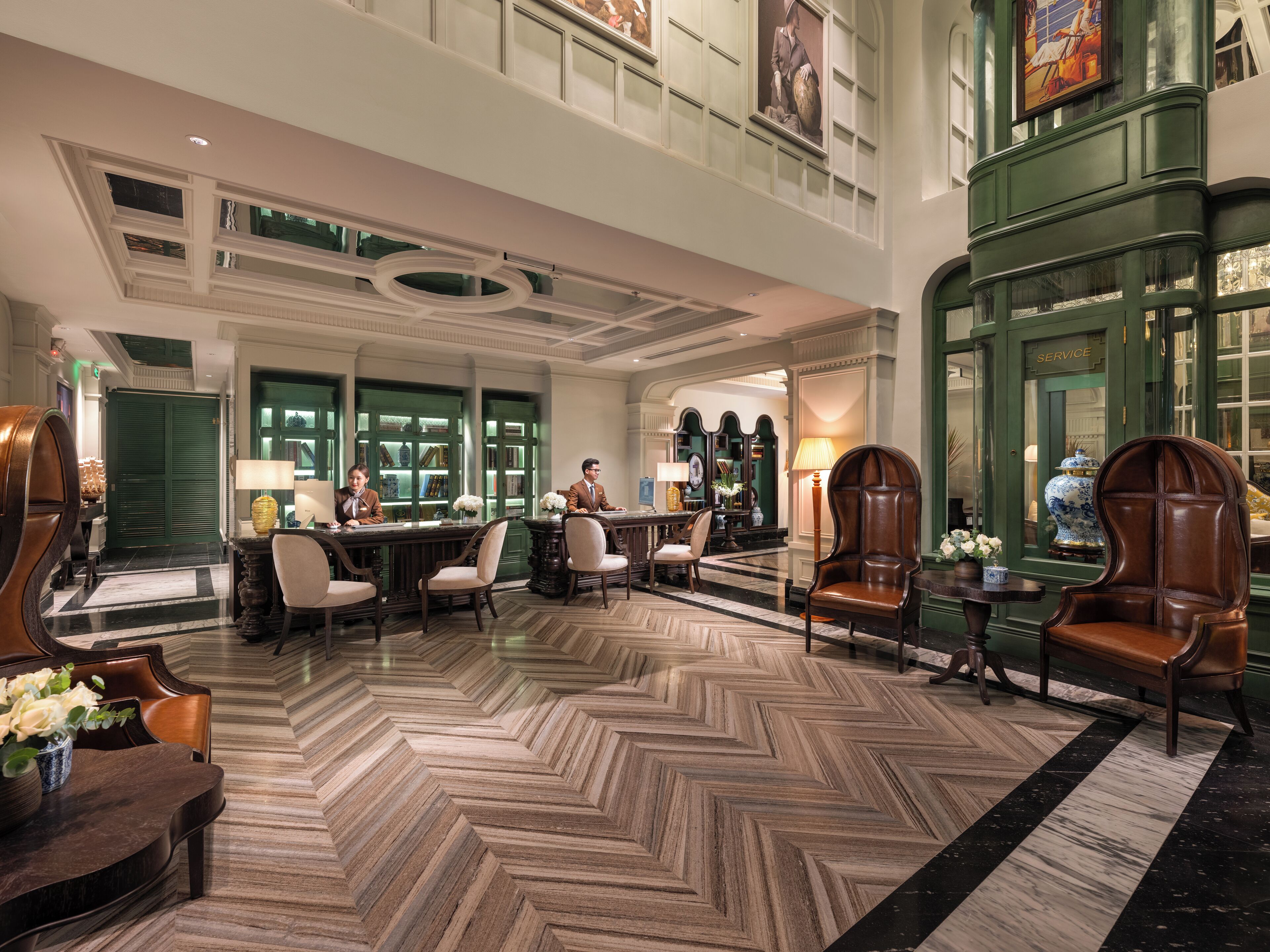 A spacious lobby with a high ceiling, a checkered floor, and a reception desk with two staff members.