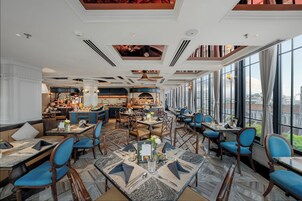 En rummelig restaurant med høje lofter, store vinduer og forskellige siddepladser, herunder borde og båse.