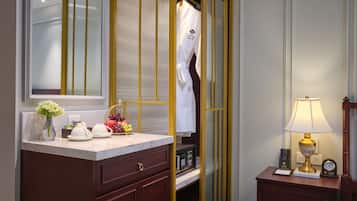 A hotel room with a vanity, a mirror, a robe, a bedside table with a lamp, and a clock.