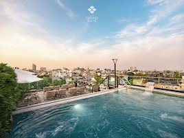 A rooftop infinity pool with a city view, lounge chairs, and a water feature.
