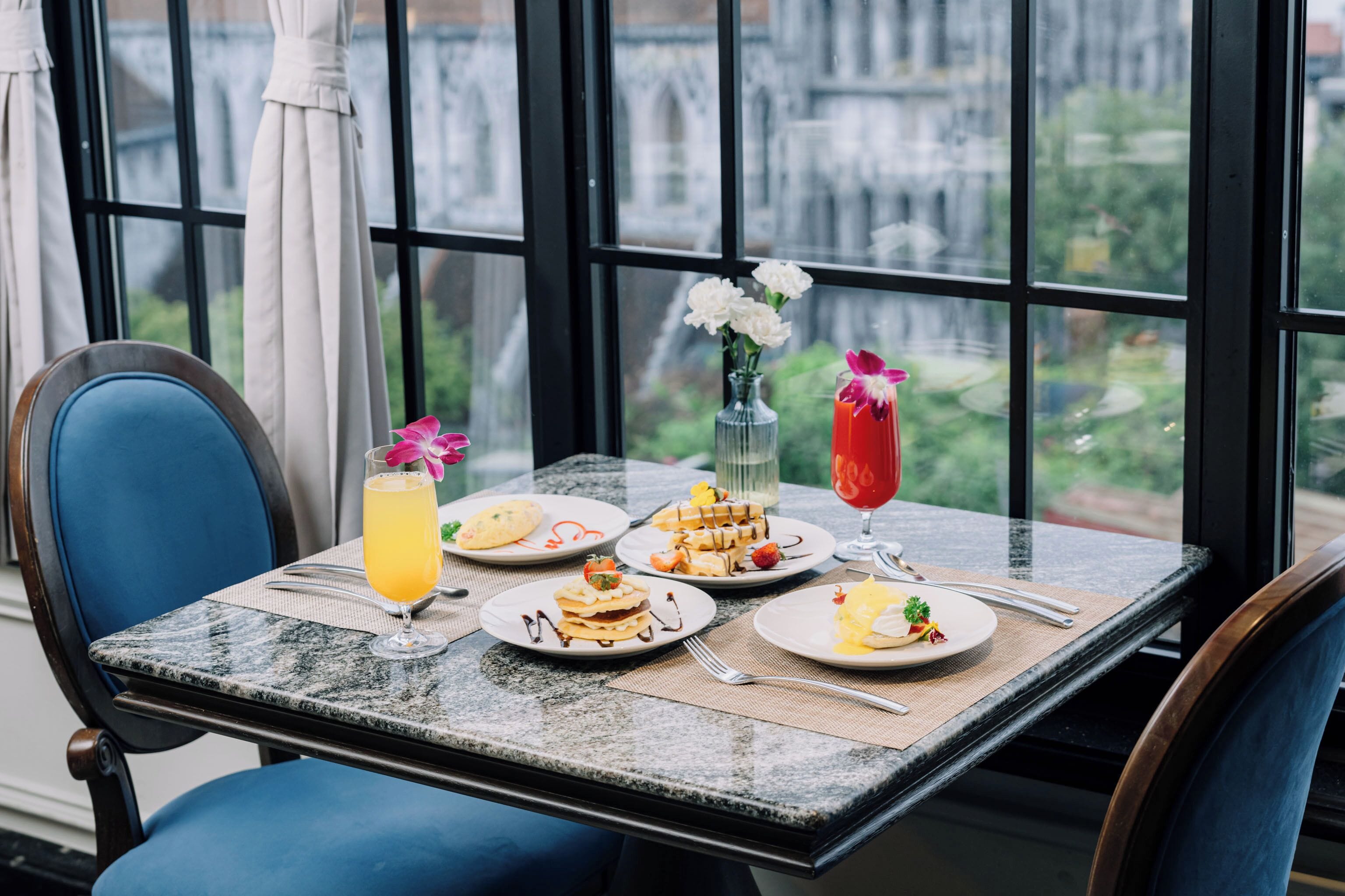 A dining table with plates of food, a glass of orange juice, and a vase with flowers.
