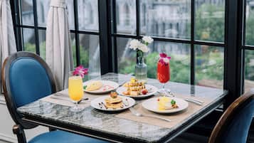 A dining table with plates of food, a glass of orange juice, and a vase with flowers.