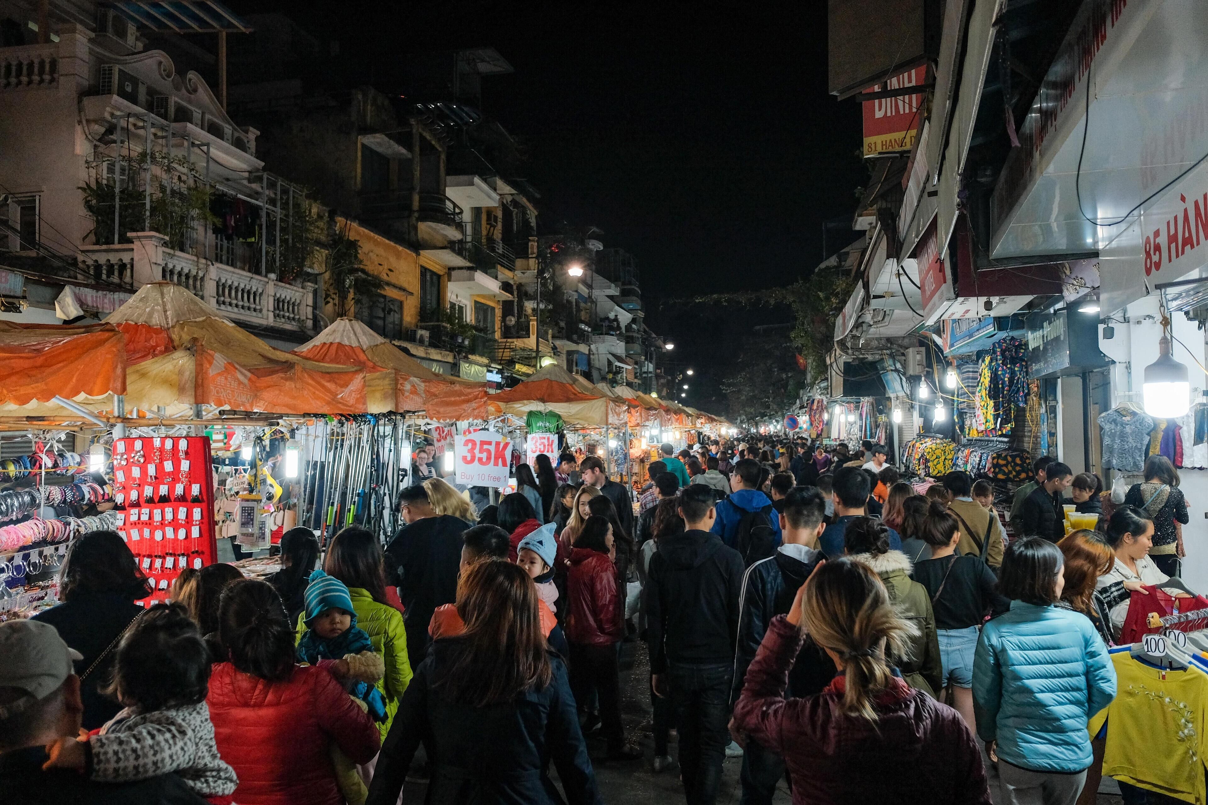 A crowded street market at night with various stalls and people.