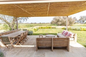 Een terras buiten met een houten tafel en stoelen, een bank en een kleine ronde tafel.