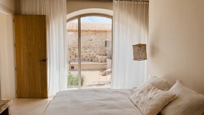Ein Schlafzimmer mit einem großen Bett, einer Holztür und Blick auf eine Terrasse mit Steinmauer und einem Stuhl.