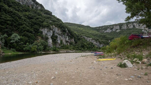 A riverbank with a rocky shore, a cliff with greenery, and several kayaks. - Caravan 'Midi - Mobil Home 6-8 Pers' with Shared Terrace and Shared Garden (Vallon-Pont-d'Arc)