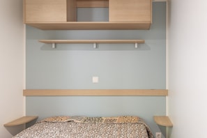 Ein Schlafzimmer mit einem Bett, einem Nachttisch, einem Regal und einem an der Wand befestigten Schrank.