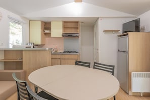 Eine kompakte Küche mit Esstisch, Stühlen, Herd, Kühlschrank und Fernseher auf einem Schrank.