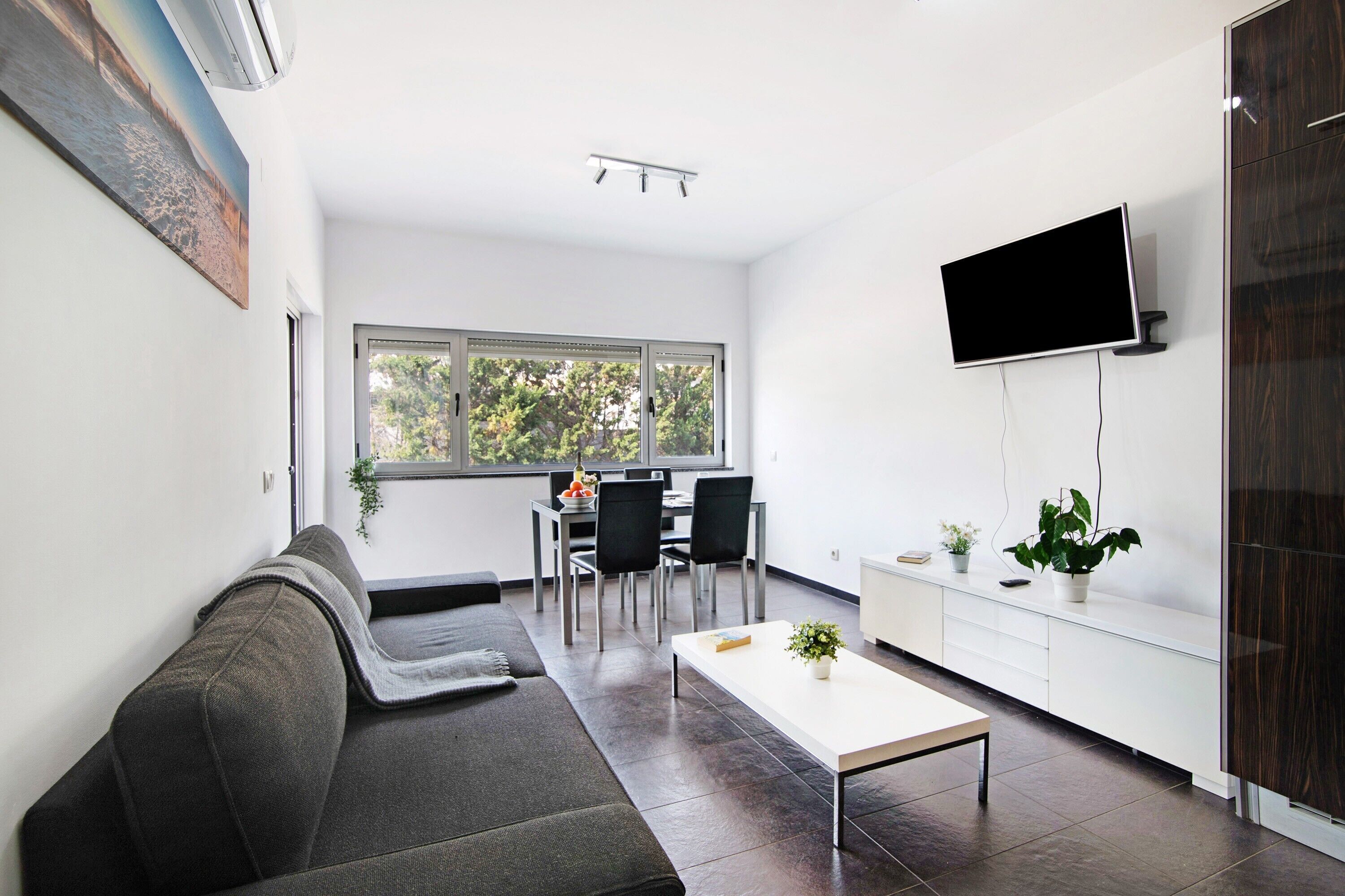 A modern living room with a sofa, a coffee table, a TV, and a dining area with chairs and a table.