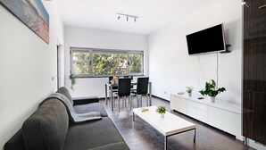 Ein modernes Wohnzimmer mit Sofa, Couchtisch, Fernseher und einem Essbereich mit Stühlen und Tisch.