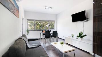 A modern living room with a sofa, a coffee table, a TV, and a dining area with chairs and a table.