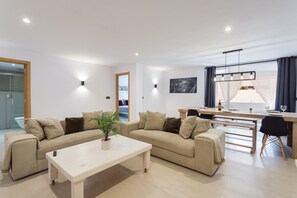 Una sala de estar moderna con un conjunto de sofás, una mesa de centro, un comedor con mesa y sillas, y un amplio ventanal con cortinas.