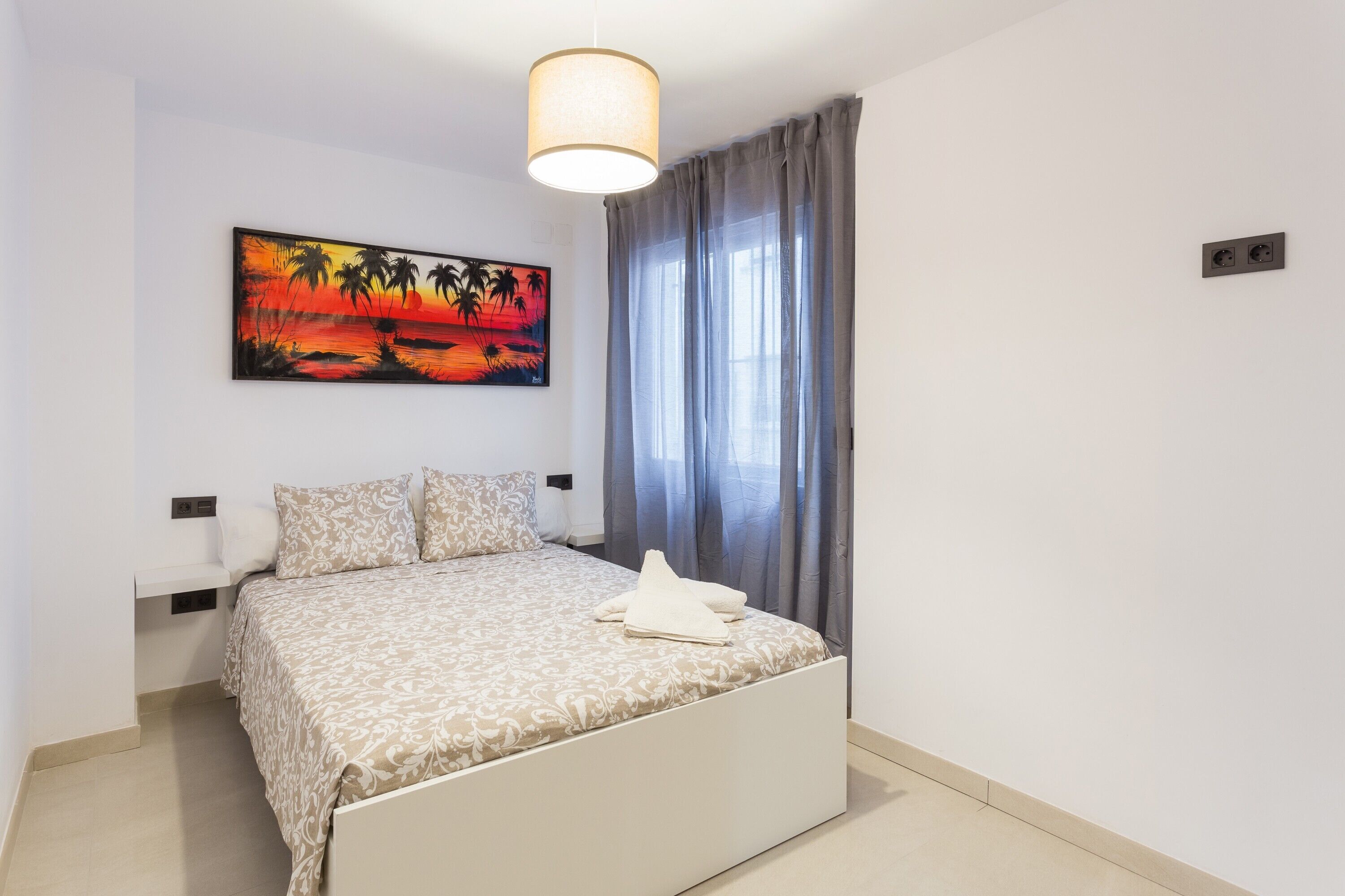 Un dormitorio con cama, un cuadro, una ventana con cortinas y una lámpara.