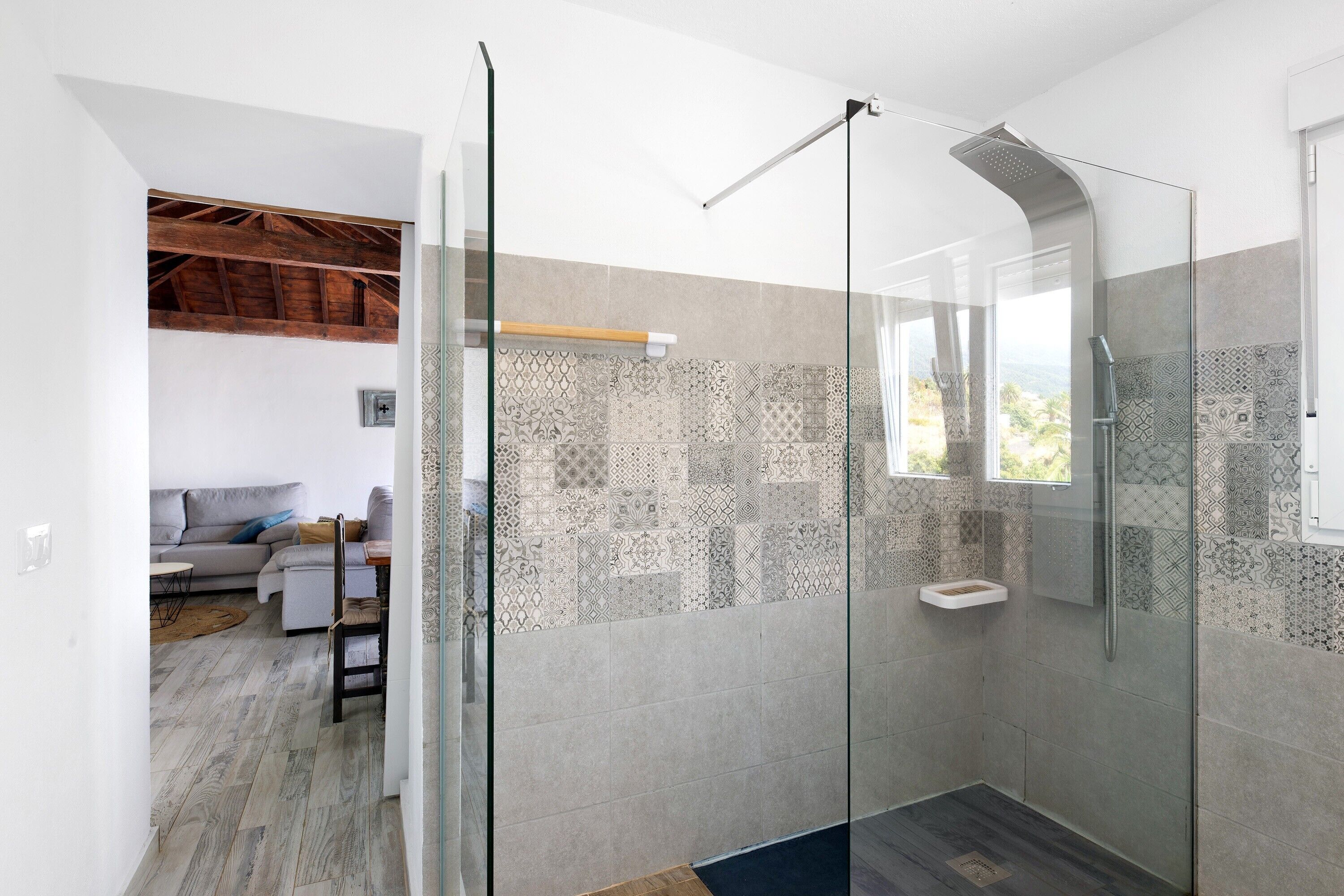 A modern bathroom with a glass shower enclosure, patterned tiles, and a view of the outdoors.
