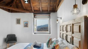 Een slaapkamer met een houten plafond, een groot raam met uitzicht, een bed met witte lakens en een stoel.