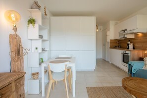 A modern kitchen with white cabinetry, a dining area with a white table and chairs, and a wooden accent wall.