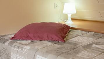 A bed with a patterned bedspread and a single red pillow.