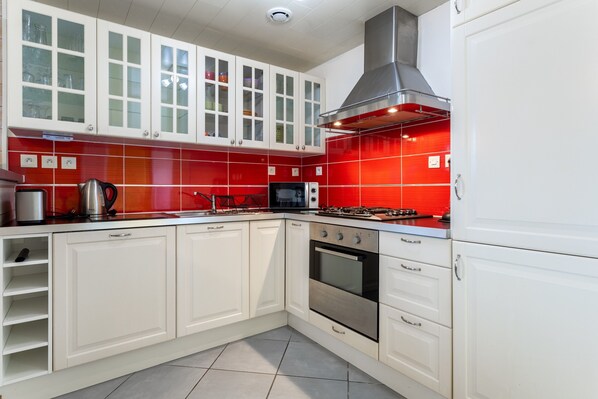 Una cocina con armarios blancos, un salpicadero rojo, electrodomésticos de acero inoxidable y una estufa a gas.