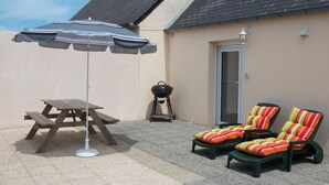 An outdoor patio with a picnic table, a barbecue grill, and two lounge chairs. - Holiday Home 'Chez Fanch' with Private Terrace, Private Garden and Wi-Fi (Camaret-sur-Mer)