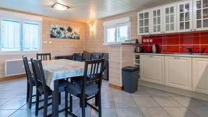 A dining area with a table and chairs, a kitchen with cabinets, and a window with curtains. - Holiday Home 'Chez Fanch' with Private Terrace, Private Garden and Wi-Fi (Camaret-sur-Mer)