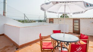 Una terraza en la azotea con una mesa de vidrio, sillas rojas y un paraguas blanco.