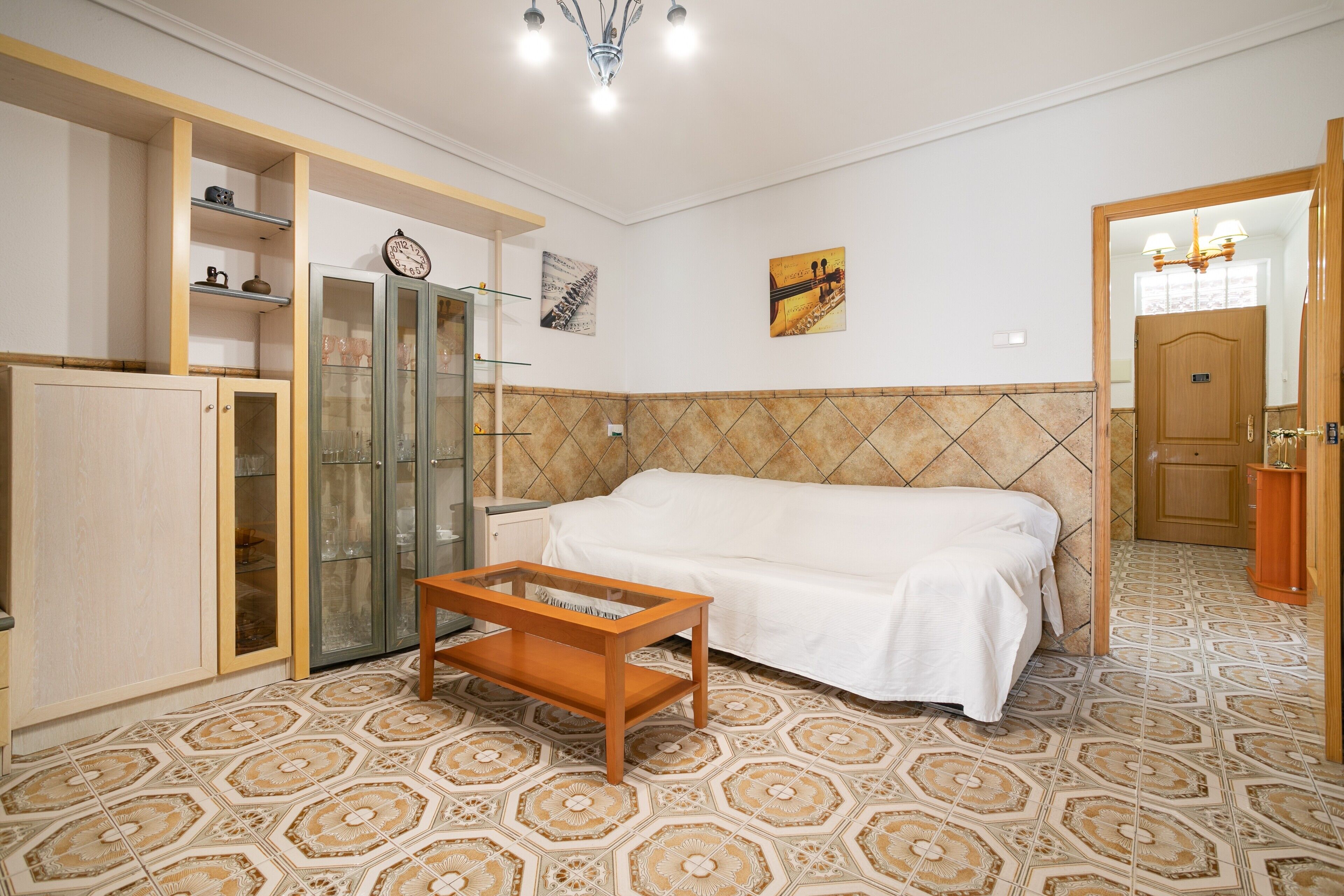Ein Zimmer mit einem Bett, einem Holztisch, einer Glasschrank und einer Tür zu einem anderen Raum.