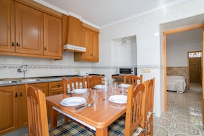 A dining area with a wooden table set for four, wooden chairs, a kitchen with a microwave, and a tiled floor.