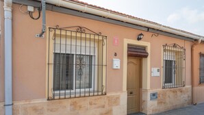 Un edificio con fachada color beige, un letrero con el número 3, ventanas protegidas con rejas y una puerta con toldo marrón.