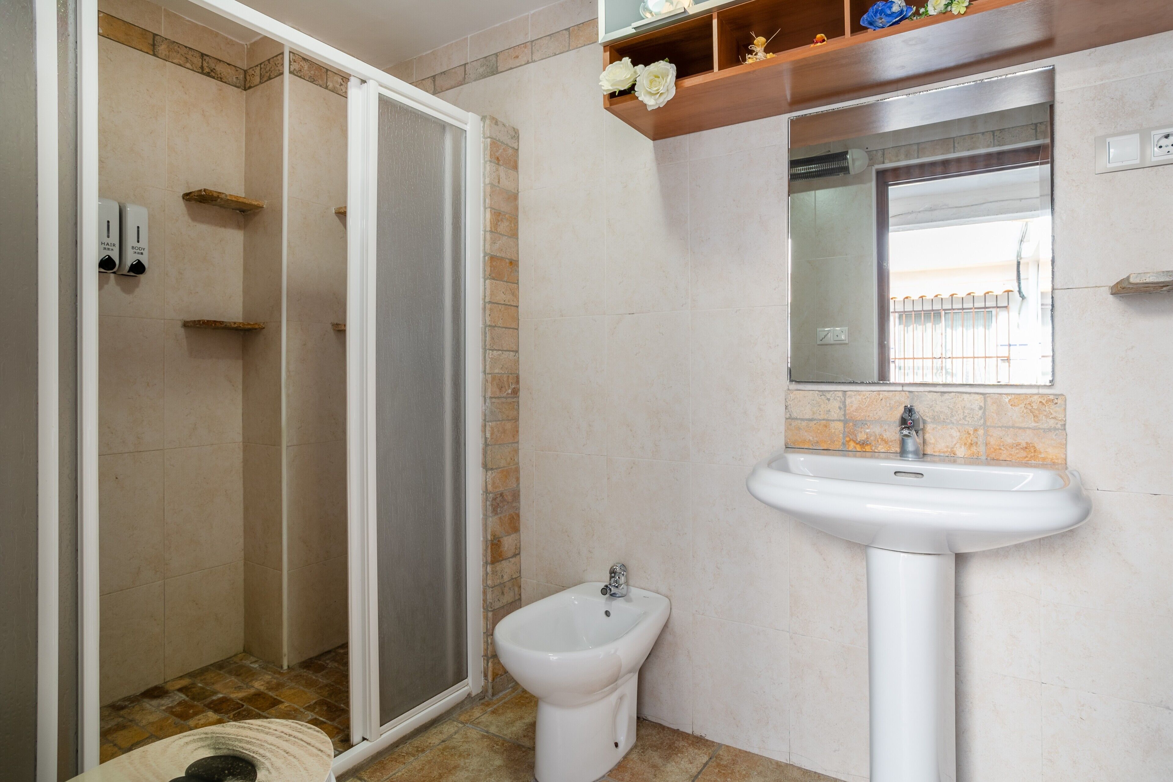 A bathroom with a shower, a bidet, a sink, and a mirror.