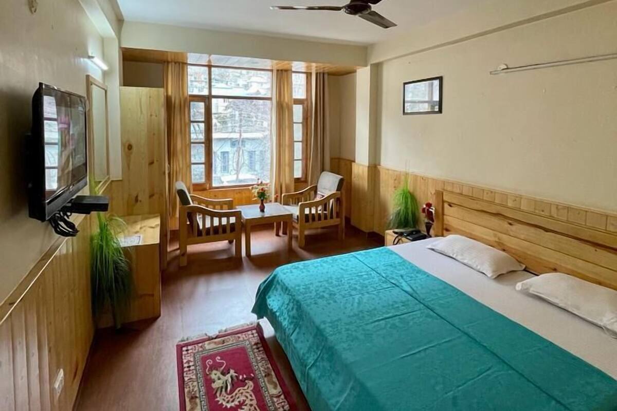 A hotel room with a bed, a desk, a chair, a television, and a window with curtains.